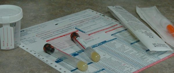 Empty vials that are used to collect blood sitting on medical paperwork