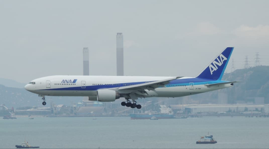 A large plane in flight. In the background, there is a skyline of a city.